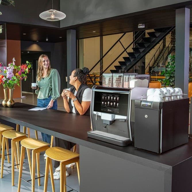 Two coworkers chatting over coffee at their office coffee bar
