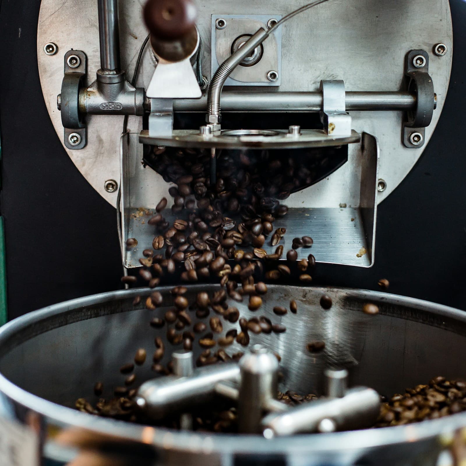 Freshly roasted whole coffee beans pouring from a commercial roaster